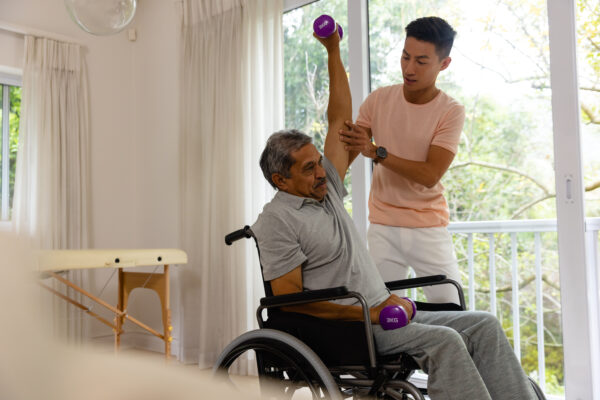 Diverse male physiotherapist advising and senior male patient in wheelchair using dumbbells. Physiotherapy, healthcare, wellbeing, and senior lifestyle, unaltered. Registered NDIS Provider Melbourne